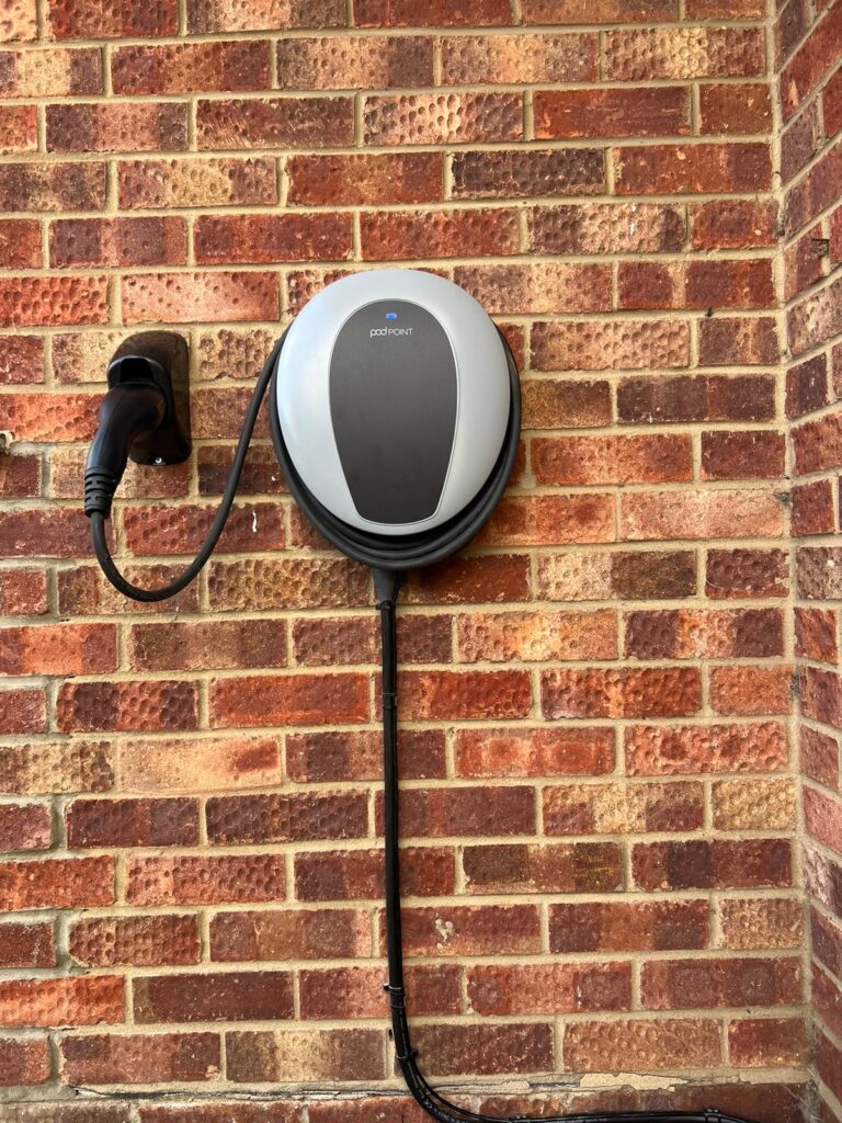 An electric vehicle charging station mounted on a brick wall with the charging cable plugged in.