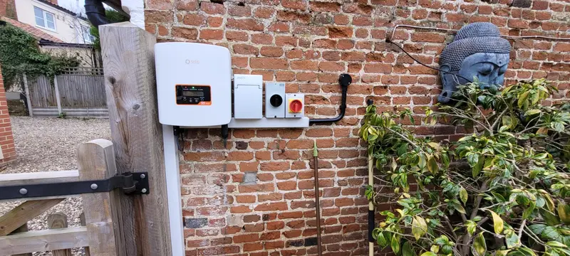 Outdoor electrical setup on a brick wall featuring a charging point and connectors, with a buddha statue and green shrubbery nearby.