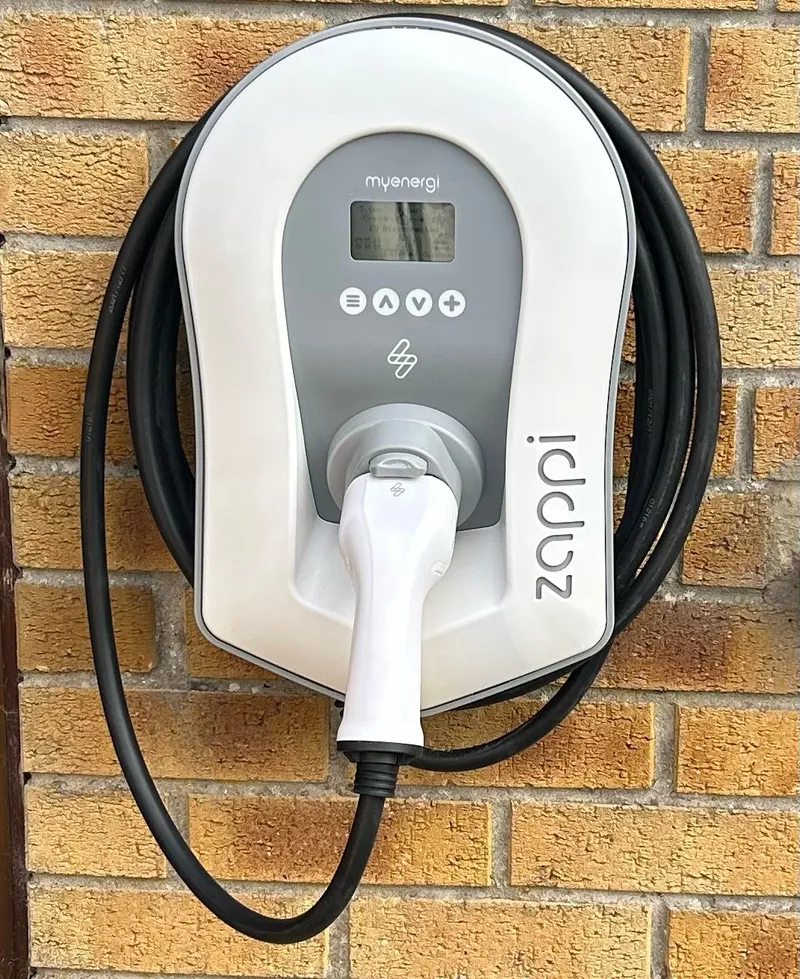 An electric vehicle charging station mounted on a brick wall, featuring a coiled charging cable and digital display.