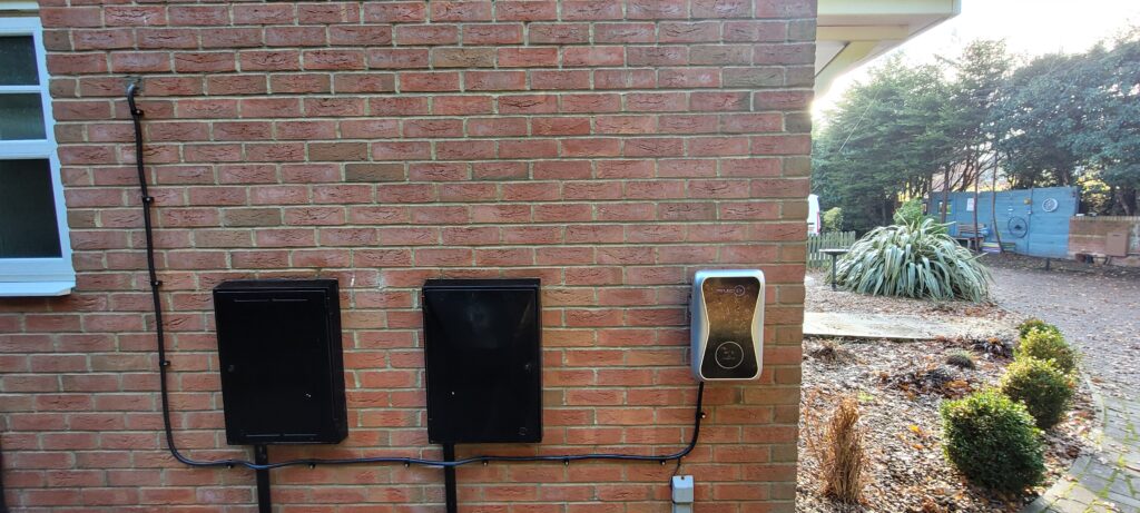 Three electrical units mounted on a brick wall, with cables running downwards, alongside a garden pathway.