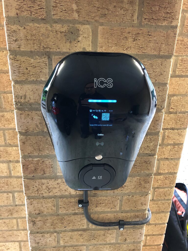 Wall-mounted electric vehicle charging station with digital display and cables, installed on a brick wall.