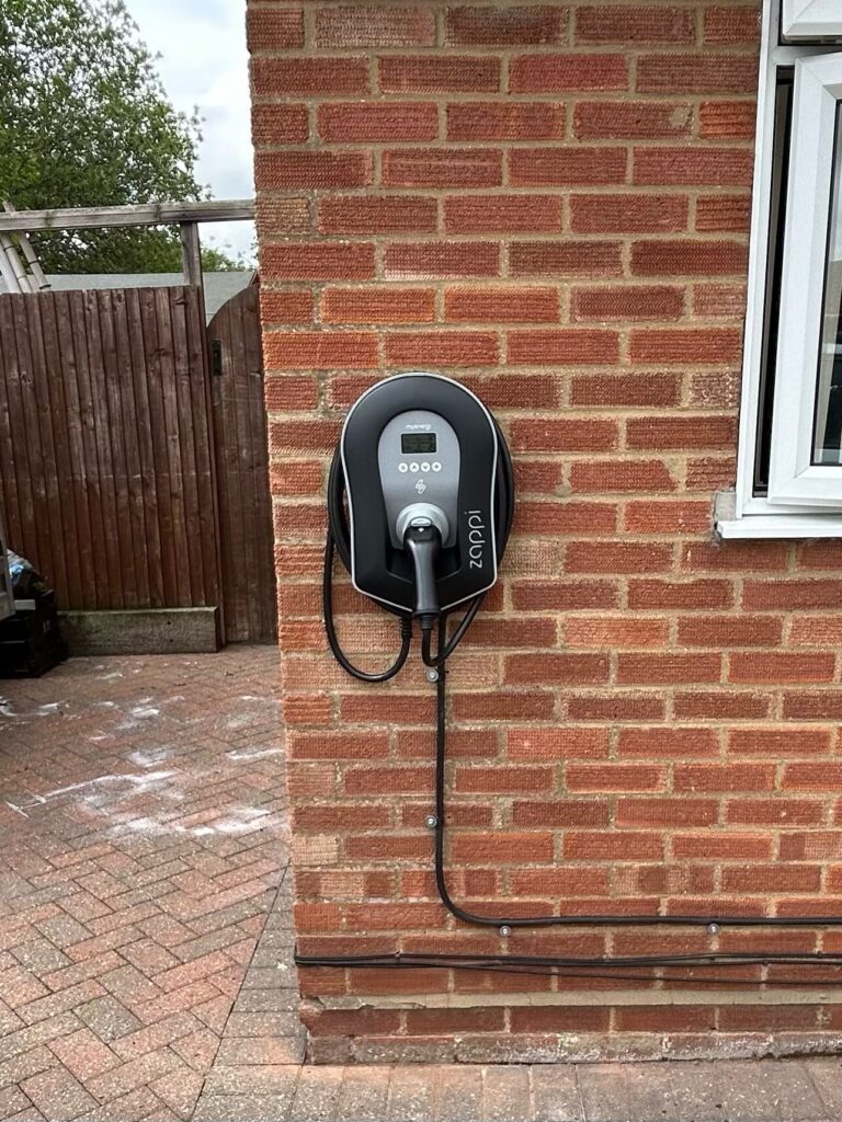 Electric car charging station mounted on a brick wall beside a house window, with a coiled charging cable.